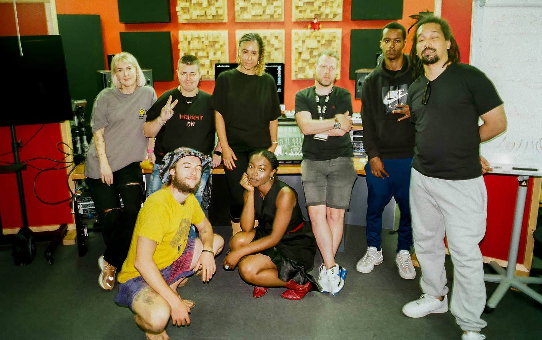 A group of students pose infront of the mixing desk in a music production training room.